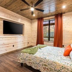Same queen bedroom with a TV set into the wall and a ceiling fan
