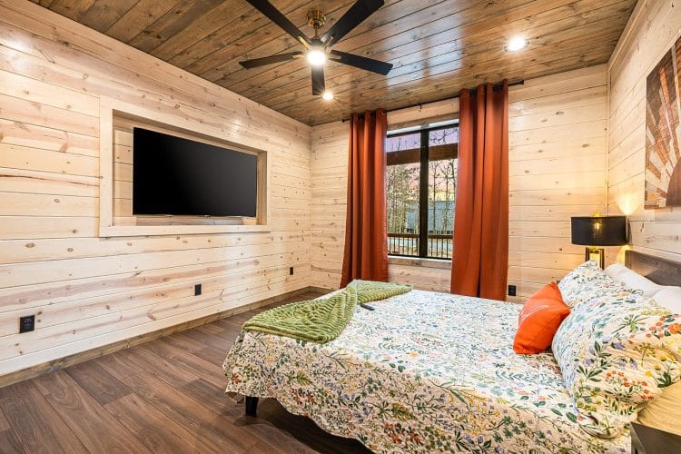 Same queen bedroom with a TV set into the wall and a ceiling fan