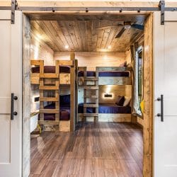 View through white barn doors into a bunk room with wood bunks