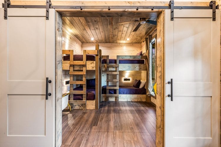 View through white barn doors into a bunk room with wood bunks