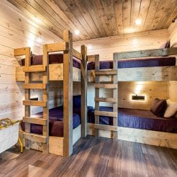 Bunk room with two sets of wood bunks with navy bedding and a luggage rack