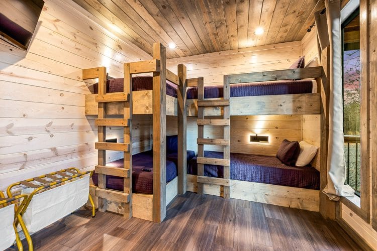Bunk room with two sets of wood bunks with navy bedding and a luggage rack