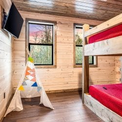 Bunk bed with red bedding and a canvas teepee, with a TV on the wall