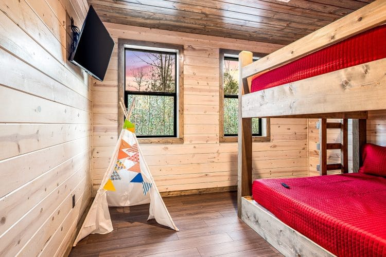 Bunk bed with red bedding and a canvas teepee, with a TV on the wall