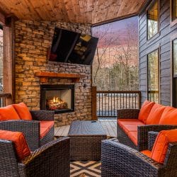 Covered patio with a stone fireplace burning, a TV and orange-cushioned wicker chairs