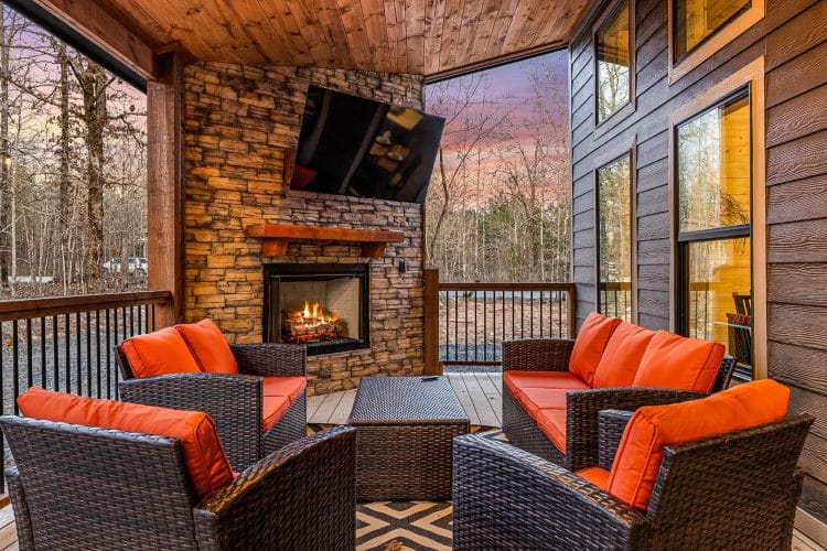 Covered patio with a stone fireplace burning, a TV and orange-cushioned wicker chairs