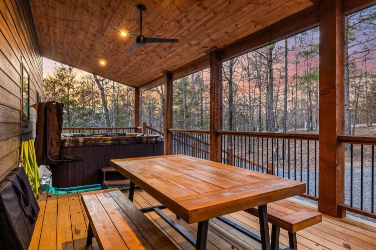 Covered deck with a wood picnic table and benches, the hot tub behind