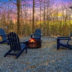 Fire pit with navy Adirondack chairs on a gravel yard at dusk