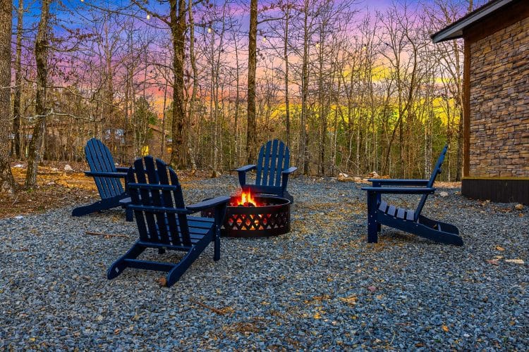 Fire pit with navy Adirondack chairs on a gravel yard at dusk
