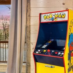 Pac-Man arcade cabinet beside a curtain and the sliding door to the deck