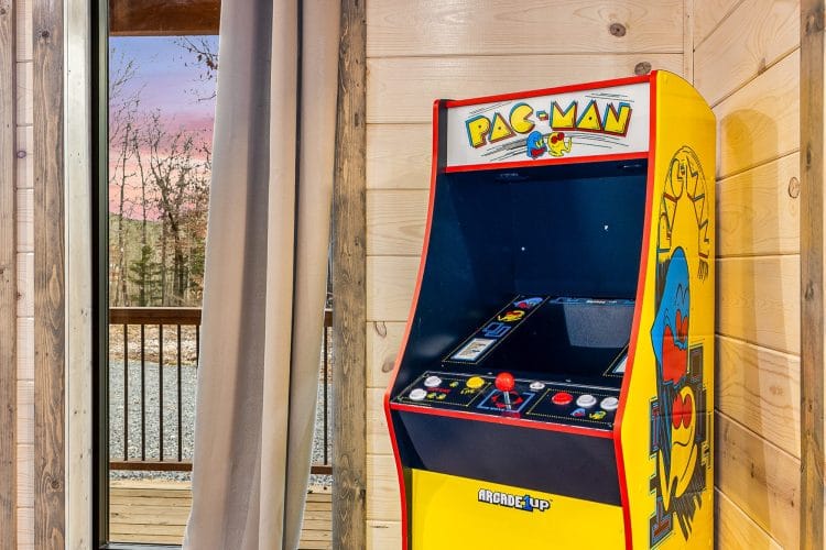 Pac-Man arcade cabinet beside a curtain and the sliding door to the deck