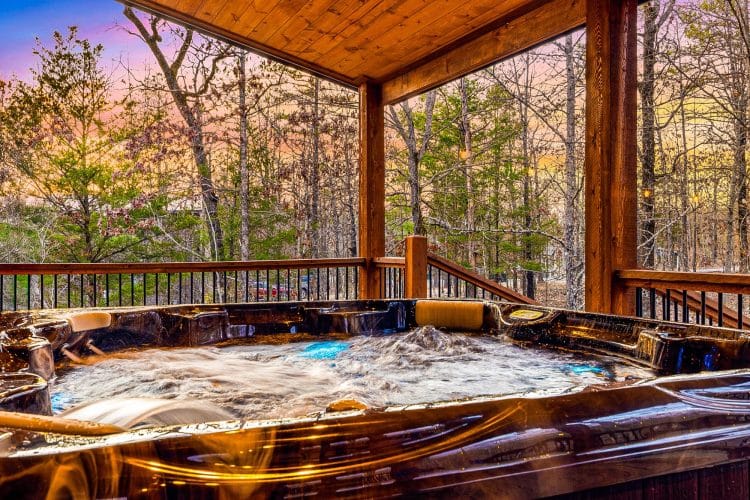 Hot tub on a covered porch at dusk with trees beyond the rail