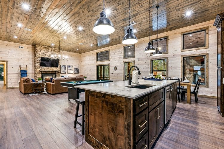Kitchen with a dark-stained island and pendant lights, the pool table beyond