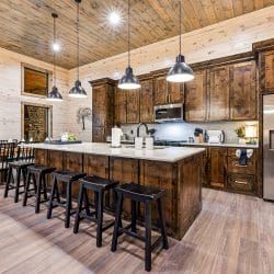 Island with black bar stools, a stainless refrigerator and pendant lights