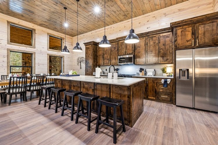 Island with black bar stools, a stainless refrigerator and pendant lights