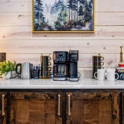 Coffee bar with a drip brewer and mugs on a white counter under a framed forest print