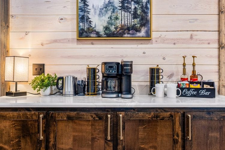 Coffee bar with a drip brewer and mugs on a white counter under a framed forest print