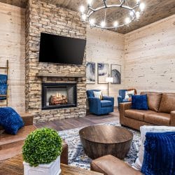 Living room with a stone fireplace, a wall TV, brown leather sofas and blue pillows