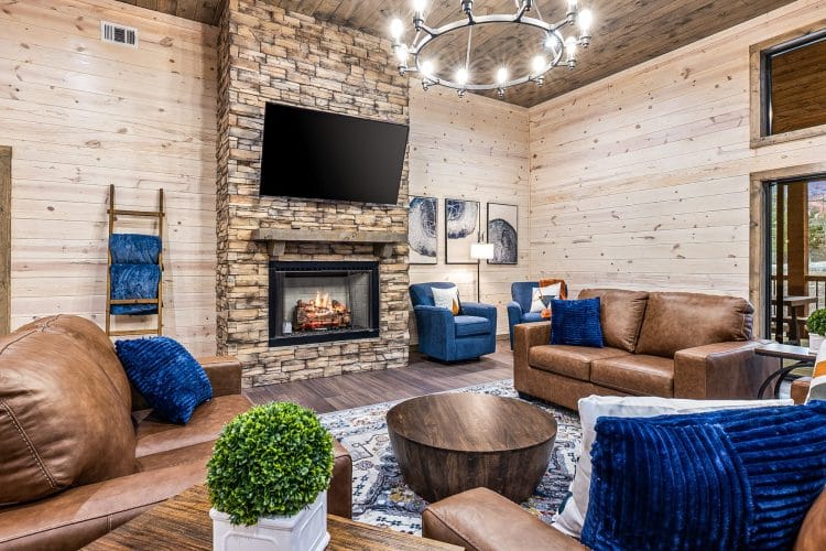 Living room with a stone fireplace, a wall TV, brown leather sofas and blue pillows