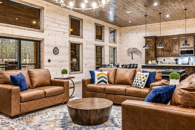 Living room with brown leather sofas, a round wood coffee table and a chandelier, the kitchen behind
