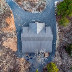 Overhead aerial of the gray roof and gravel drive at the edge of the woods