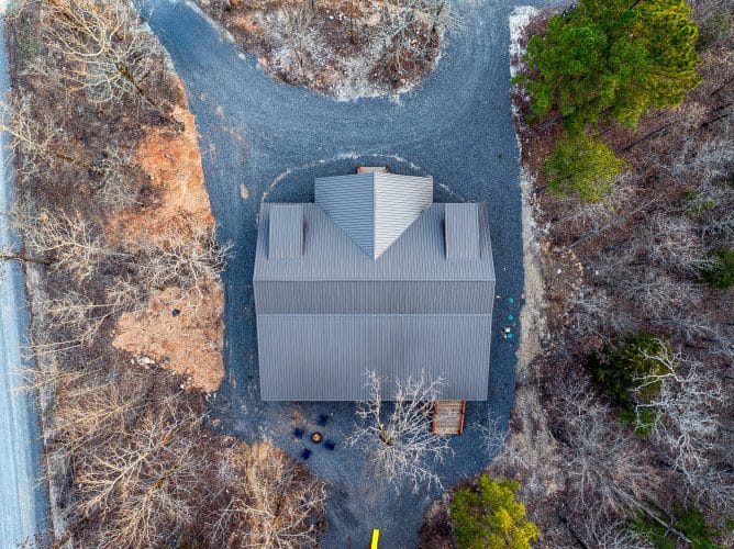 Overhead aerial of the gray roof and gravel drive at the edge of the woods