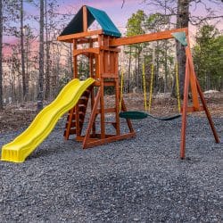 Playset with a yellow slide and swings on a gravel yard