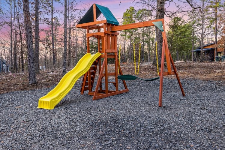 Playset with a yellow slide and swings on a gravel yard