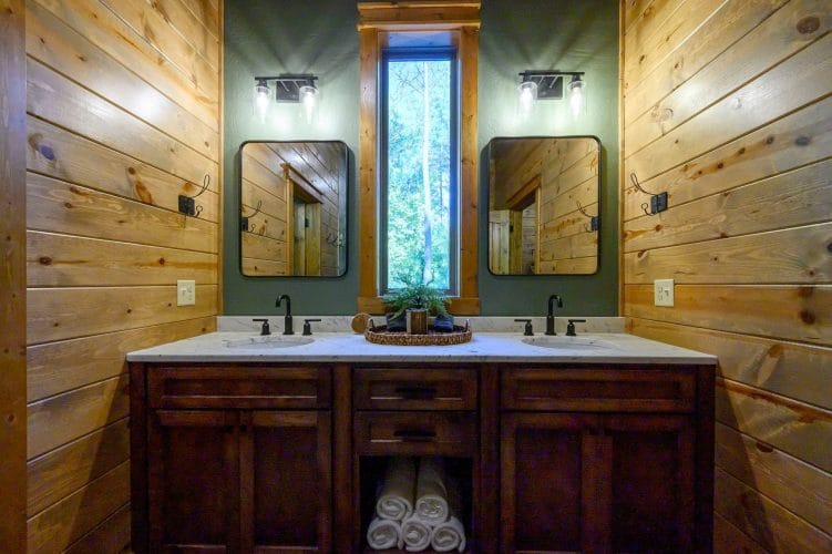 Double vanity with dark wood cabinets and two mirrors against green walls