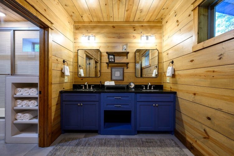 Double vanity with navy cabinets and a black top, towel shelves at the left