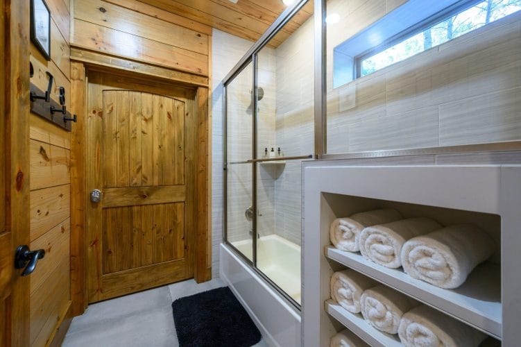 Glass-door tub-and-shower with folded towels on built-in shelves