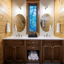 Double vanity with oval mirrors and rolled towels on an open shelf