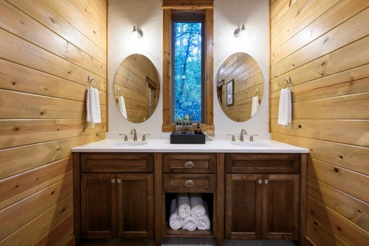 Double vanity with oval mirrors and rolled towels on an open shelf
