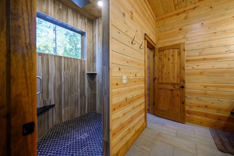 Walk-in shower with a dark hex-tile floor beside the bathroom door