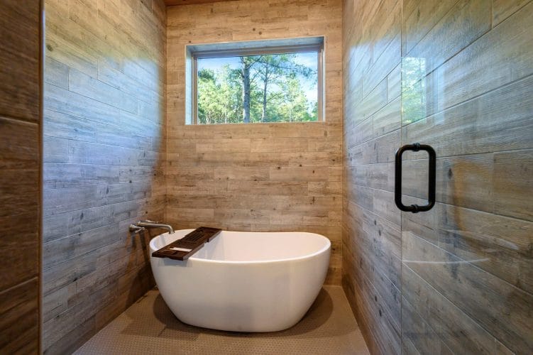 Freestanding white soaking tub beside a glass-door shower and a window