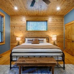 King bed with a dark metal footboard and wood bench, window above the bed