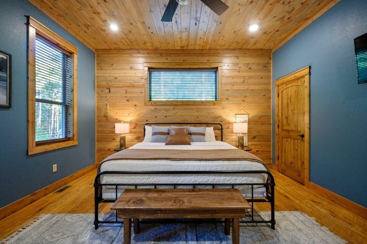 King bed with a dark metal footboard and wood bench, window above the bed