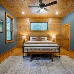 King bed with a dark metal frame and wood bench on a gray rug, TV on the right wall