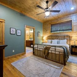 Iron-frame bed with a bench and a door to the bathroom, blue-green wall