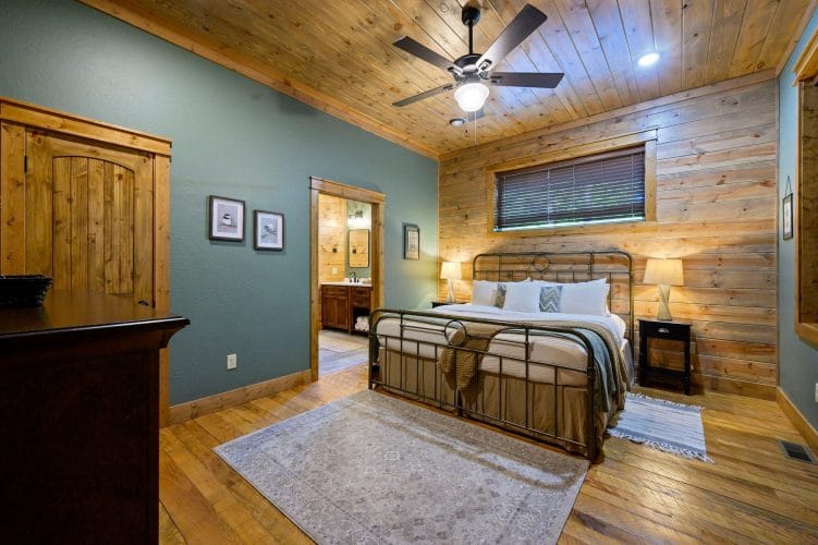 Iron-frame bed with a bench and a door to the bathroom, blue-green wall