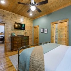 Foot of the iron bed with teal throw, TV and dresser, hallway through the open door