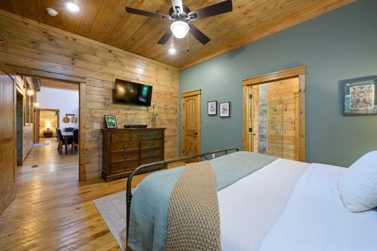 Foot of the iron bed with teal throw, TV and dresser, hallway through the open door