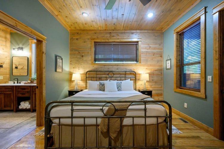 King bed with an antique-style iron frame, lamps and a bathroom doorway on the left