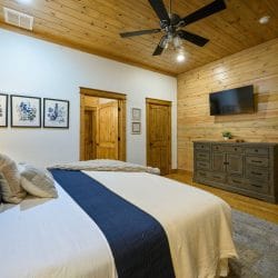 Bed with a navy runner beside a TV, framed botanical prints and a dresser