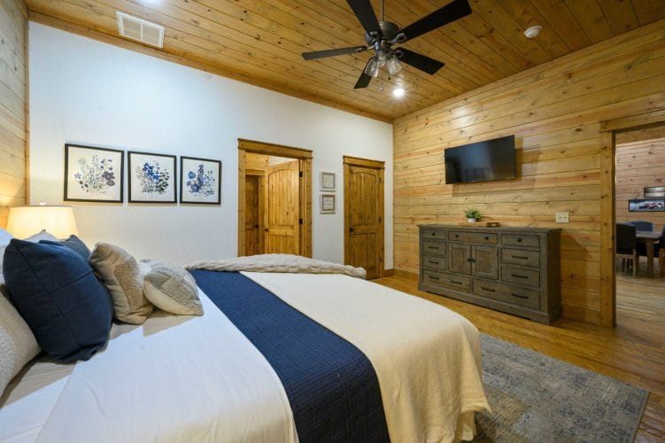 Bed with a navy runner beside a TV, framed botanical prints and a dresser