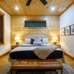 King bed with a white upholstered headboard, lamps and a leather bench at the foot