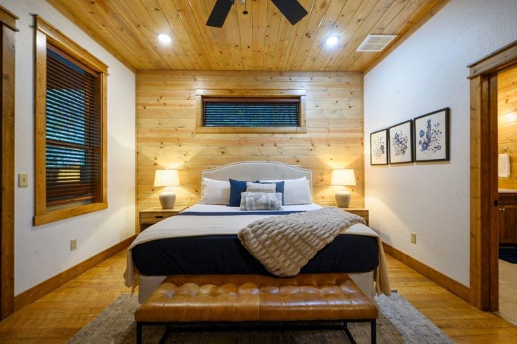 King bed with a white upholstered headboard, lamps and a leather bench at the foot