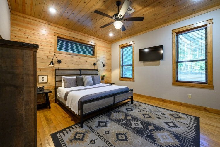 King bed with a gray and black metal frame on a patterned rug, TV on the wall
