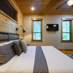 King bed with a metal headboard and gray runner, TV and two windows behind