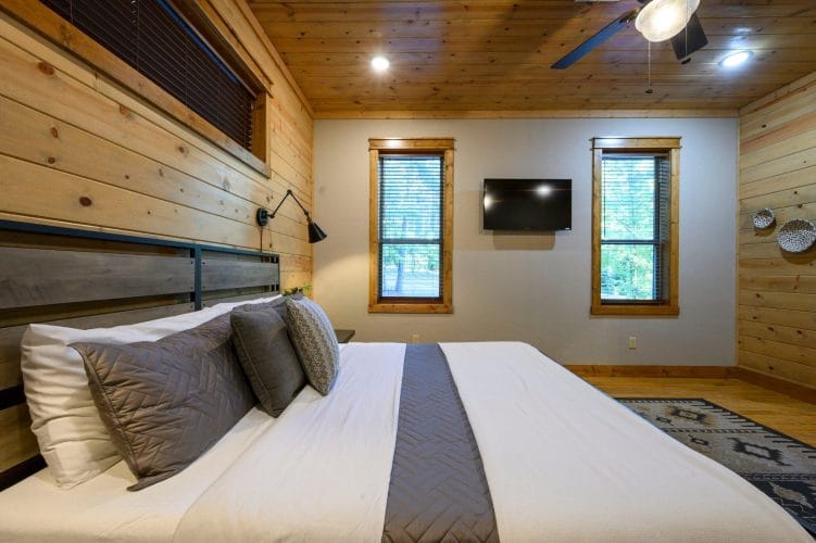 King bed with a metal headboard and gray runner, TV and two windows behind